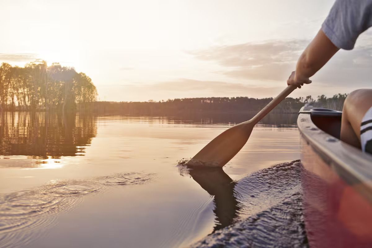 A person is paddling a canoe on a lake at sunset.