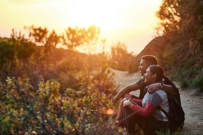 A man and a woman are sitting on a dirt road at sunset.