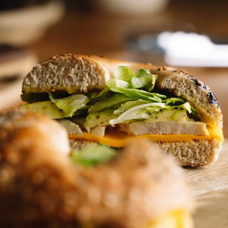 A close up of a bagel sandwich with lettuce and cheese on a table.