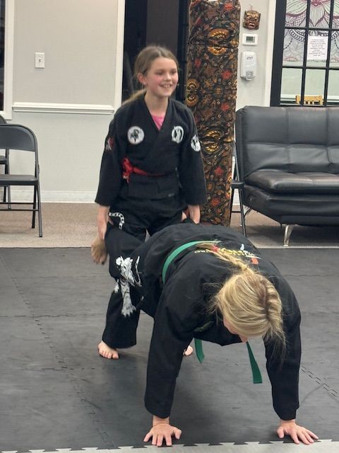 Two girls in karate uniforms are doing a handstand on a mat