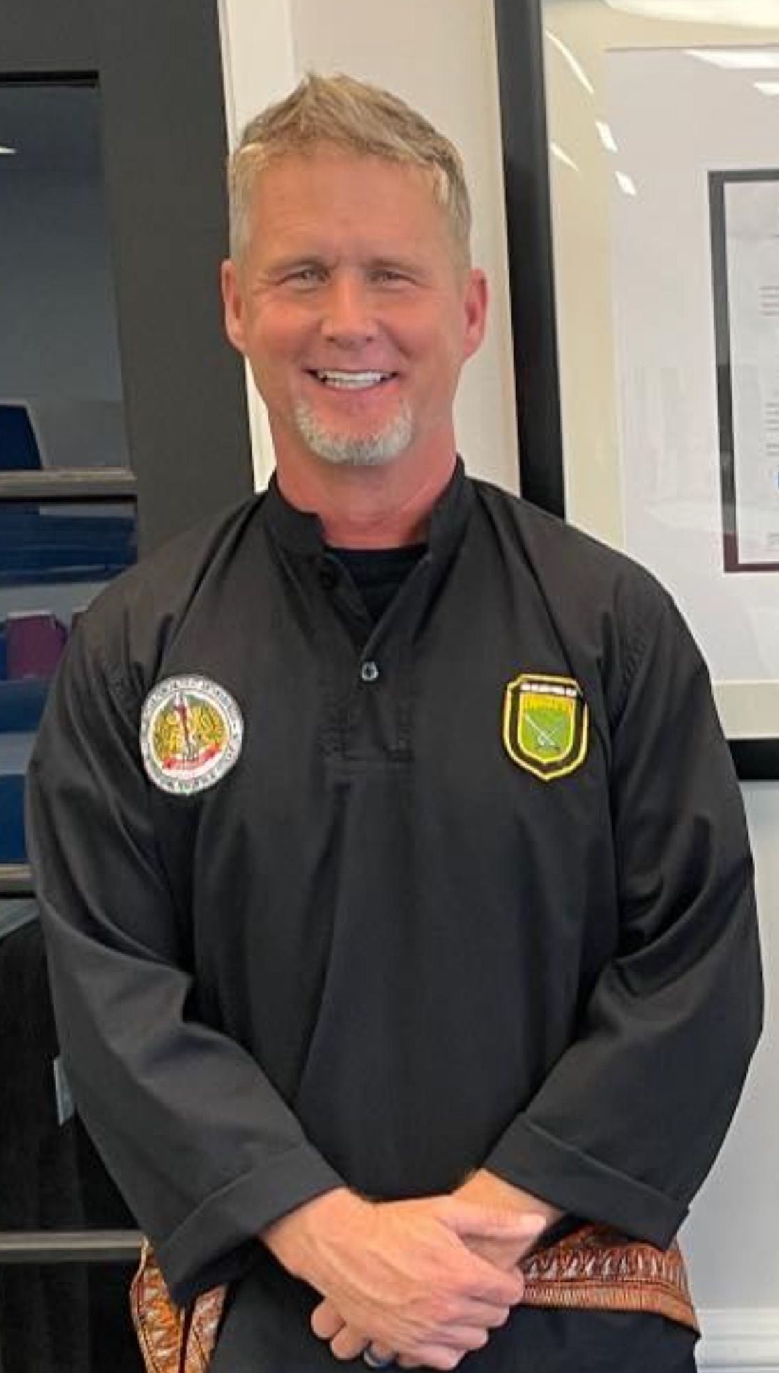 A man with a beard is wearing a black shirt and smiling.