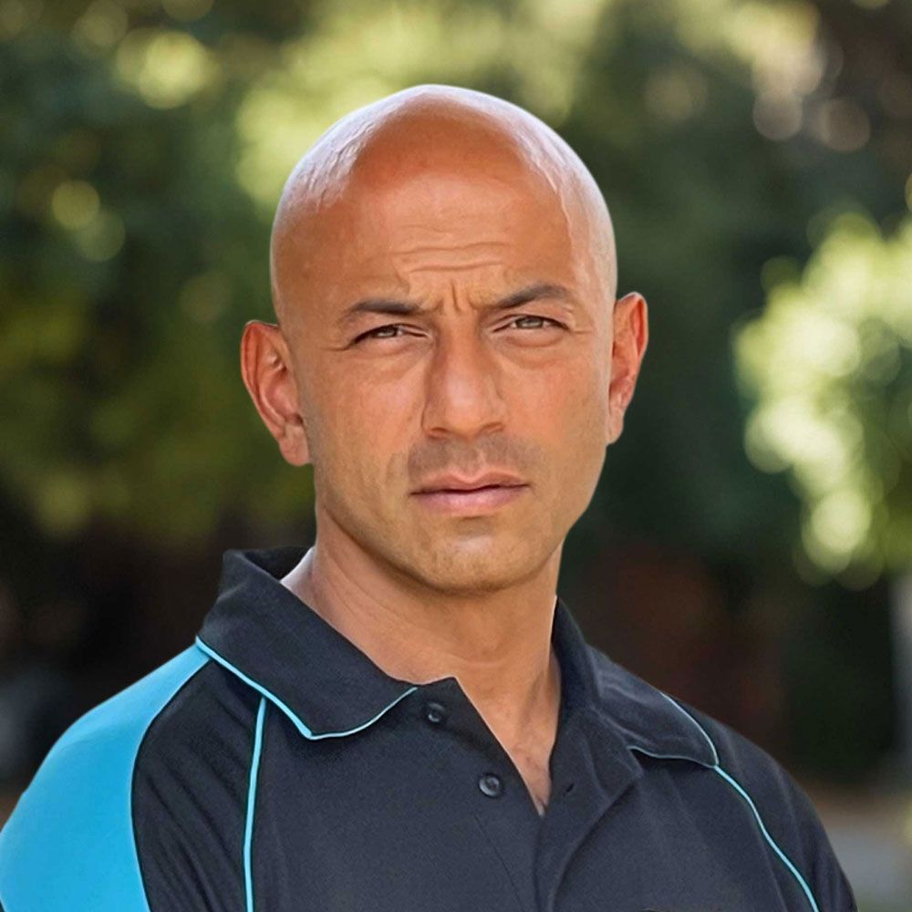 A man wearing a black and blue polo shirt is looking at the camera.