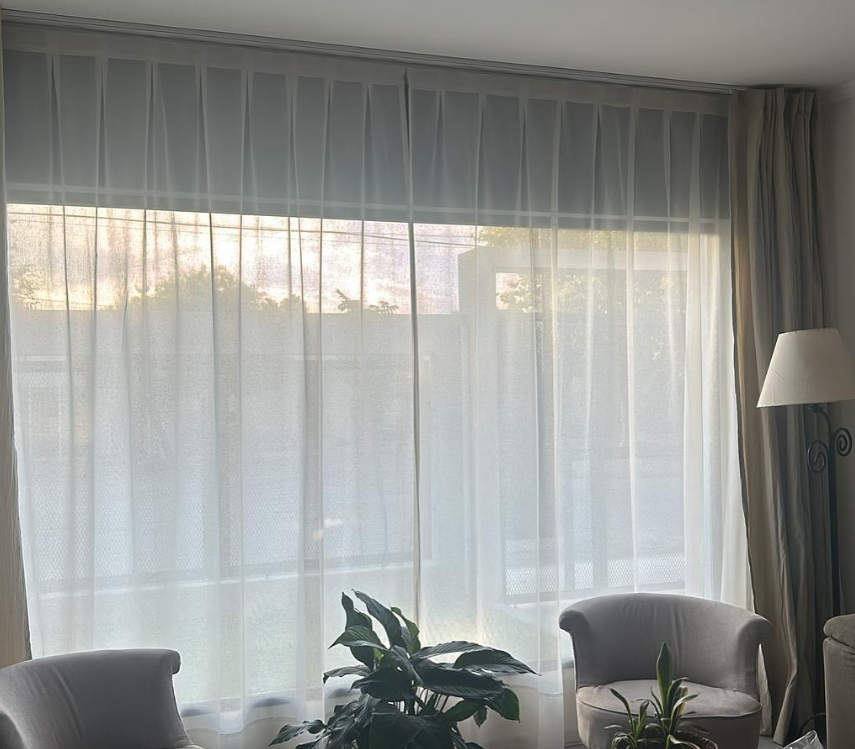 Una gran ventana con cortinas blancas translúcidas permite ver el exterior
