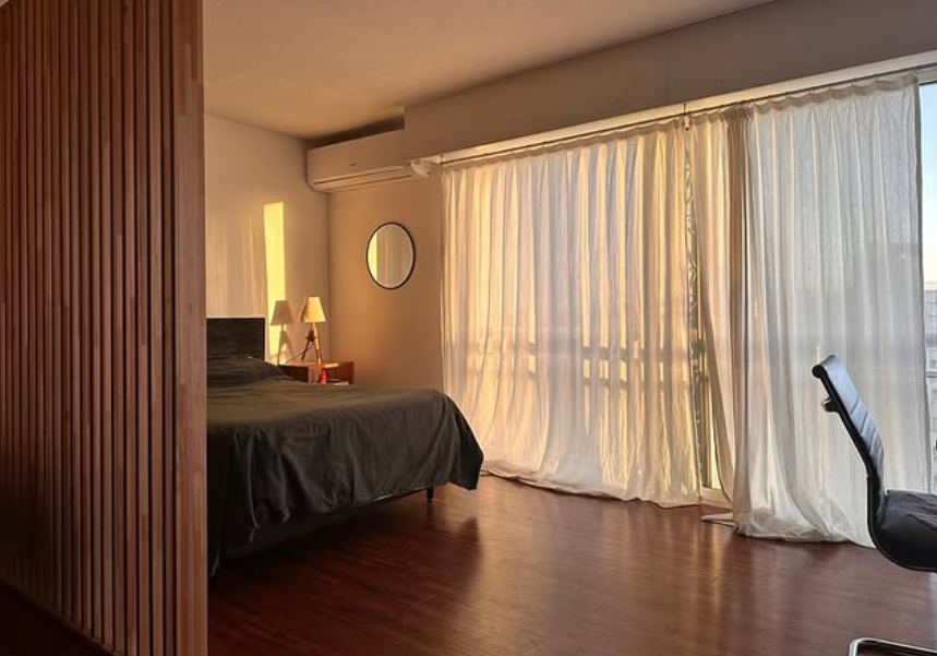 Dormitorio con pared de listones de madera, cama, cortinas transparentes y luz solar.