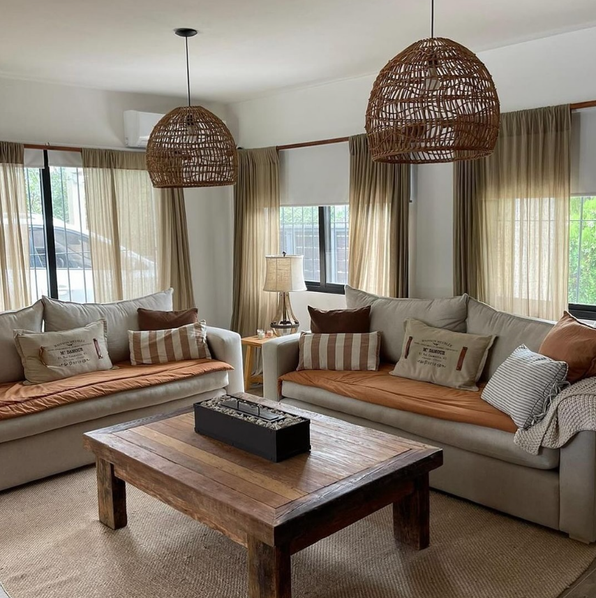 Sala de estar con dos sofás, mesa de café de madera, lámparas tejidas y cortinas color canela.