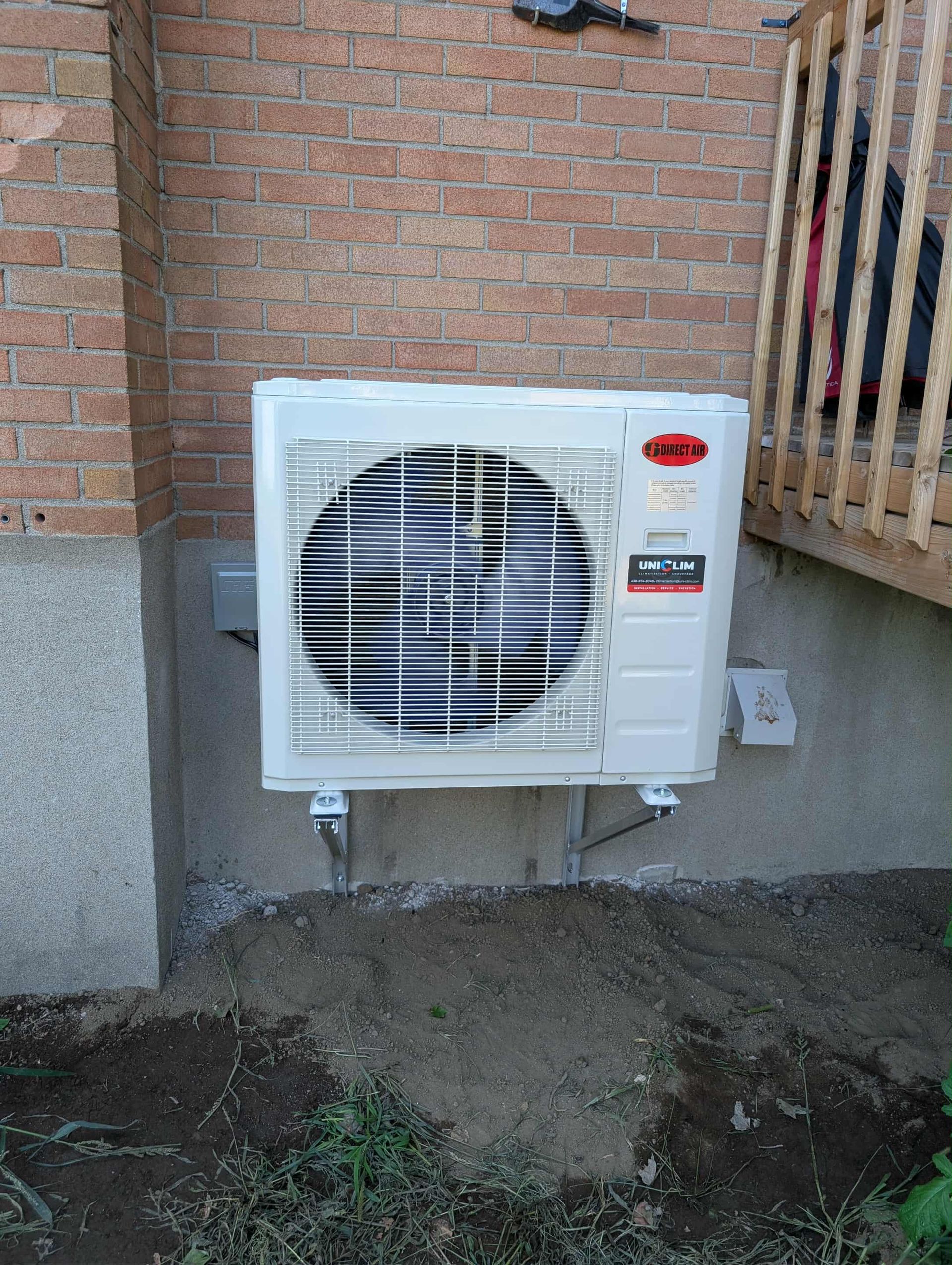 Unité de climatisation montée sur un mur de briques, à l'extérieur, avec de la terre et de l'herbe au niveau du sol en dessous.