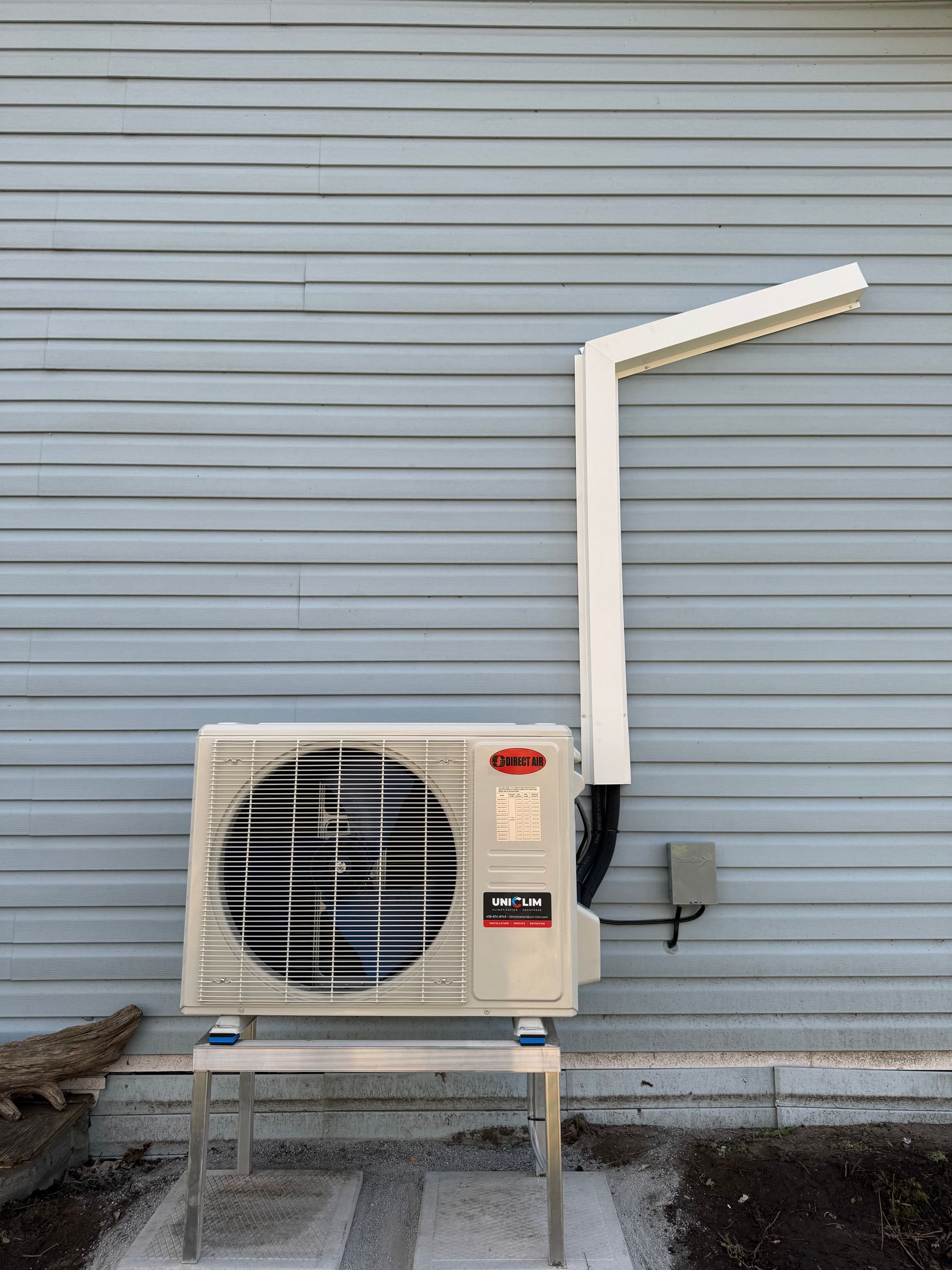 Unité de climatisation montée sur un support contre un mur à revêtement horizontal, avec un conduit s'étendant vers le haut.