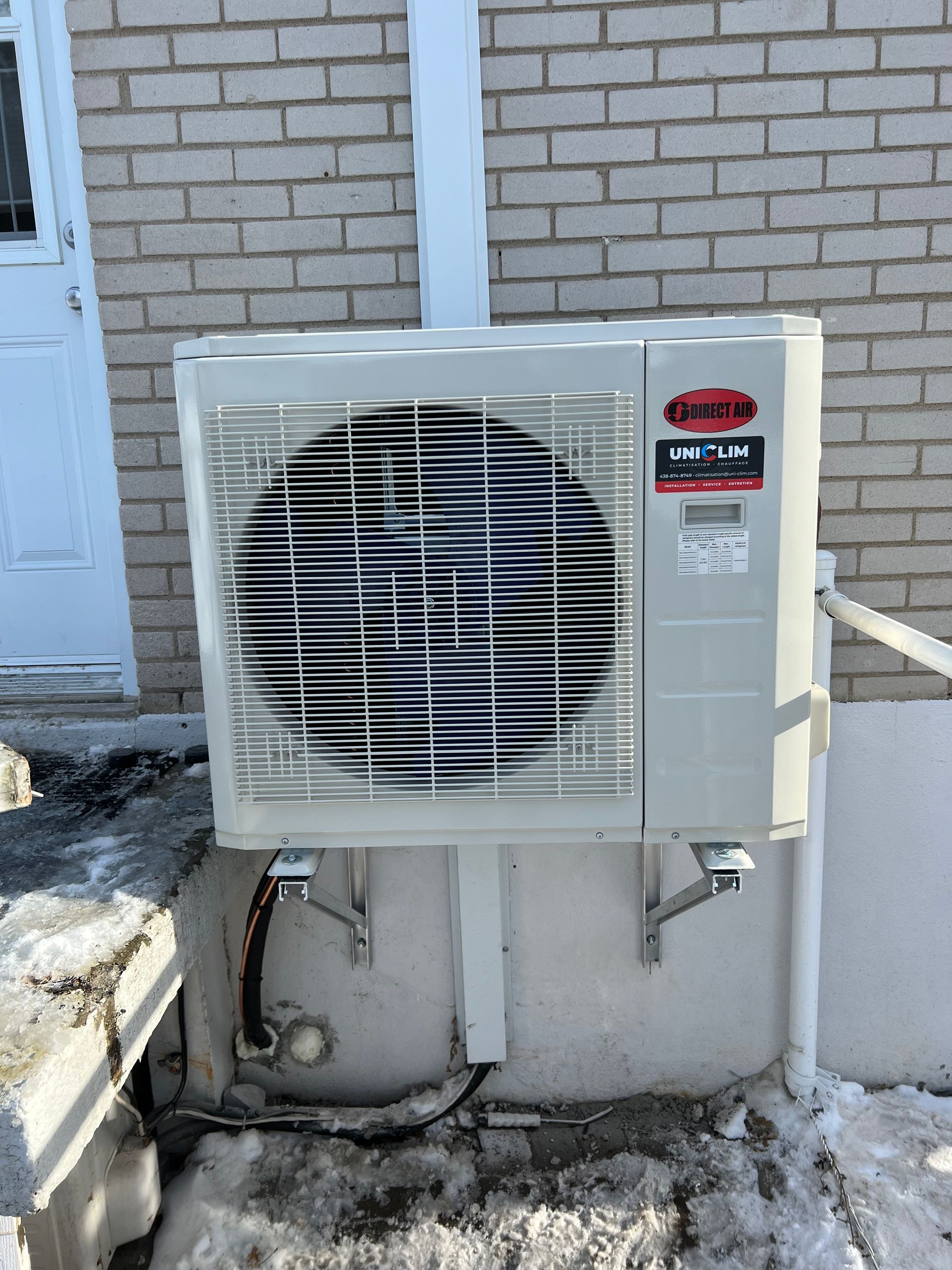 Unité de climatisation murale à l'extérieur d'un bâtiment en briques, recouverte de neige.