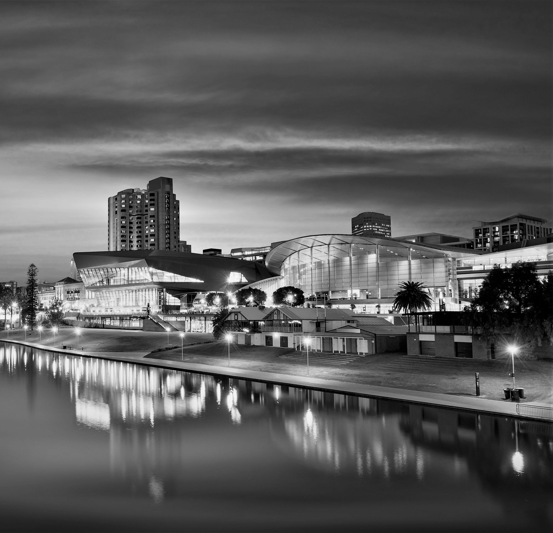 A black-and-white view of the Adelaide Convention Centre and River Torrens at dusk, with city lights reflected in the water.