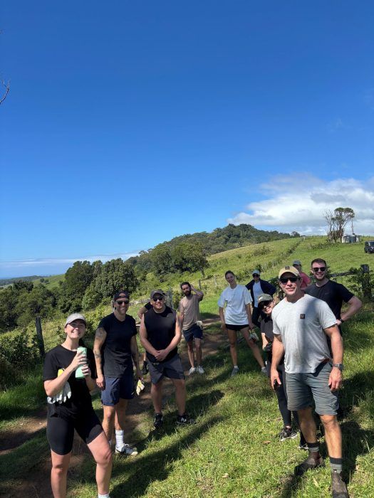 A group of people standing on a grassy hillside under a clear blue sky on a bright, sunny day.