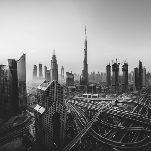Black and white aerial view of the Dubai skyline with the Burj Khalifa and a complex highway interchange.