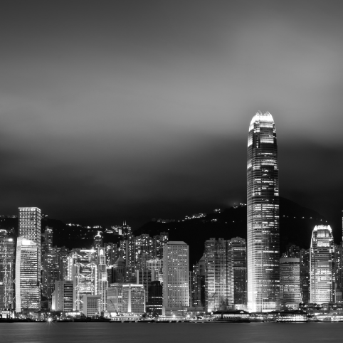 Black and white cityscape of Hong Kong’s skyline at night, featuring illuminated skyscrapers along the Victoria Harbour.