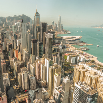 Aerial view of dense skyscrapers in Hong Kong overlooking the harbor and coastline on a clear day.