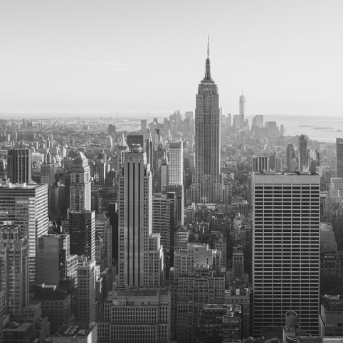A high-angle, black-and-white view of the dense New York City skyline, featuring the Empire State Building prominently.
