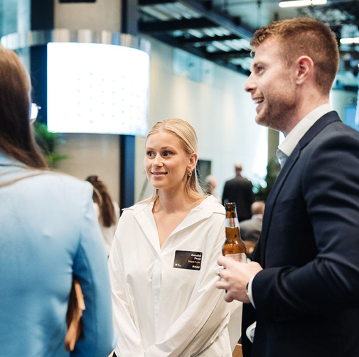 Three people in professional attire chat in a well-lit office space during a networking event.