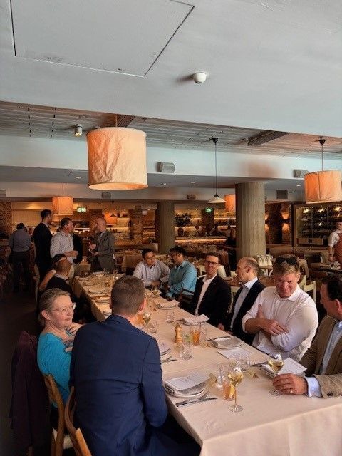 A group of people sit around a long, white-clothed table at a restaurant for a social gathering or business meal.