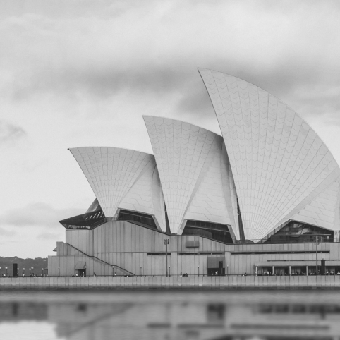 A black-and-white view of the iconic Sydney Opera House with its distinct white sails against a cloudy sky.