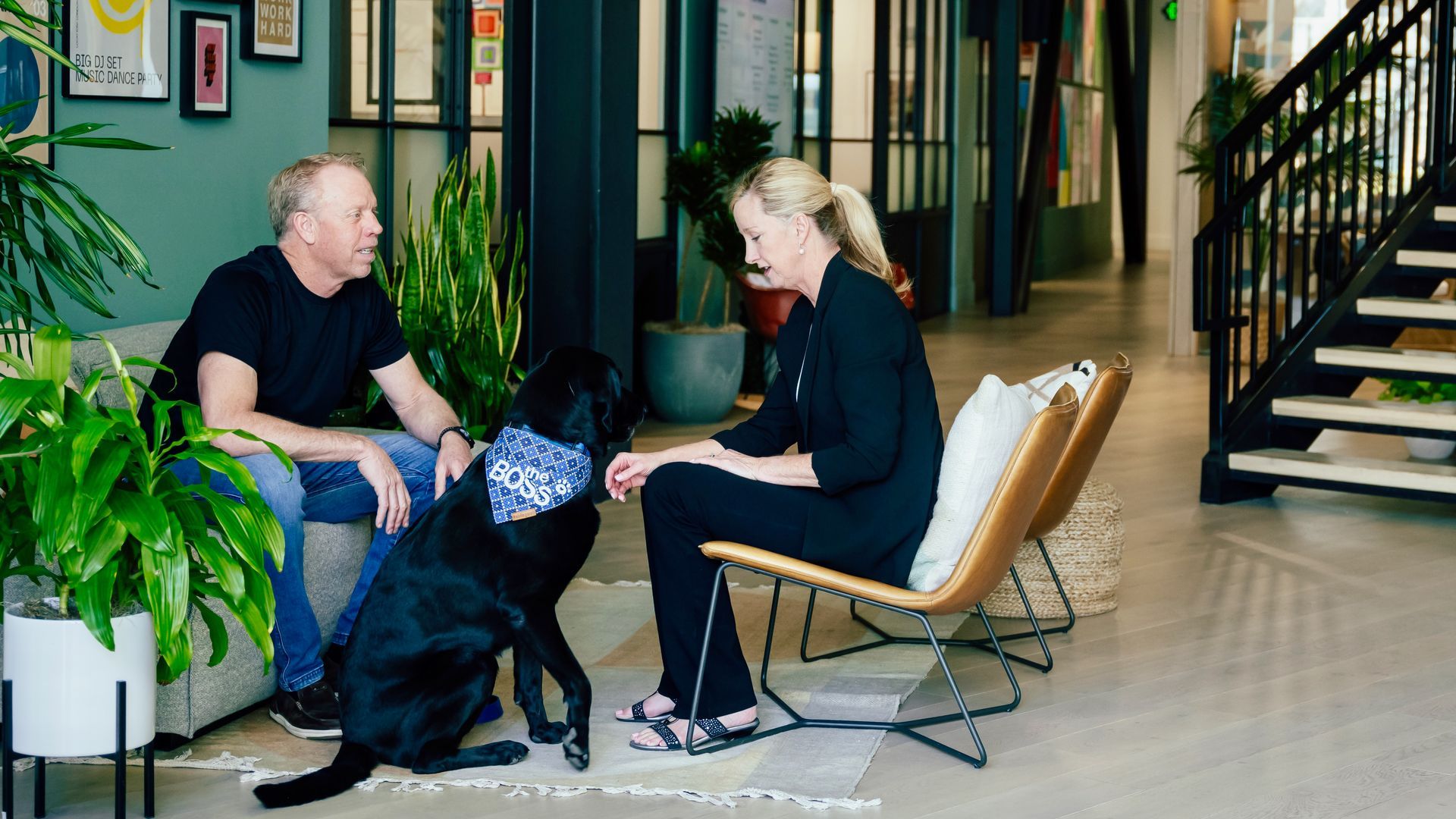 A man and a woman are sitting on a couch with a black dog.