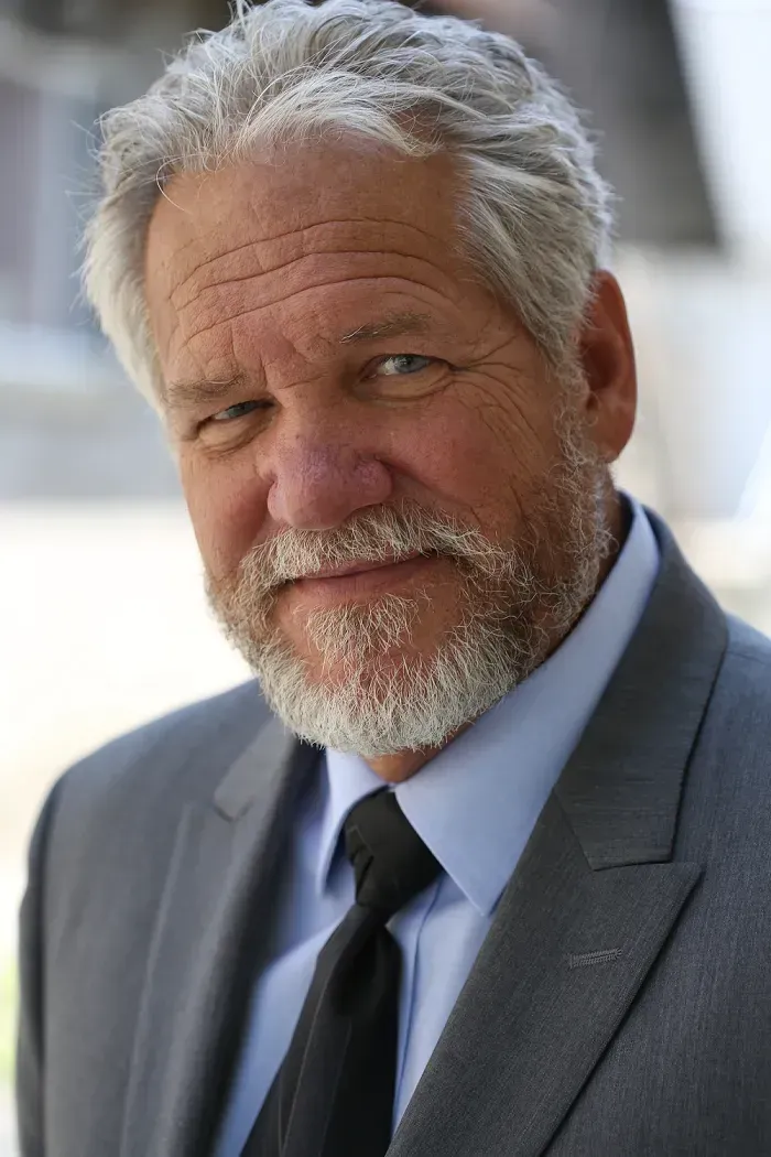 A man with a beard is wearing a suit and tie and smiling.