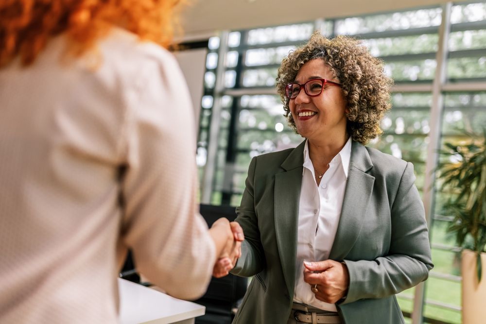 A woman in a suit is shaking hands with another woman in an office.