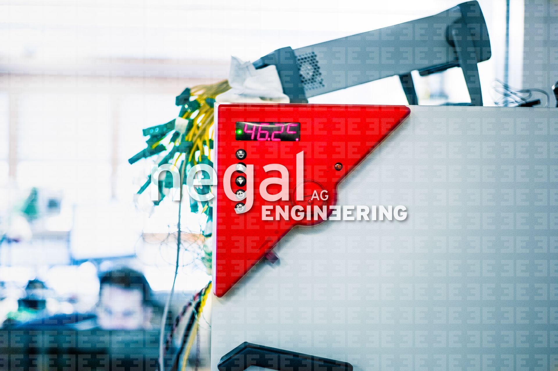 Rotes Bedienfeld mit 96,2 auf einer weissen Maschine. Im unscharfen Hintergrund sind eine Person und eine Ausrüstung zu sehen.