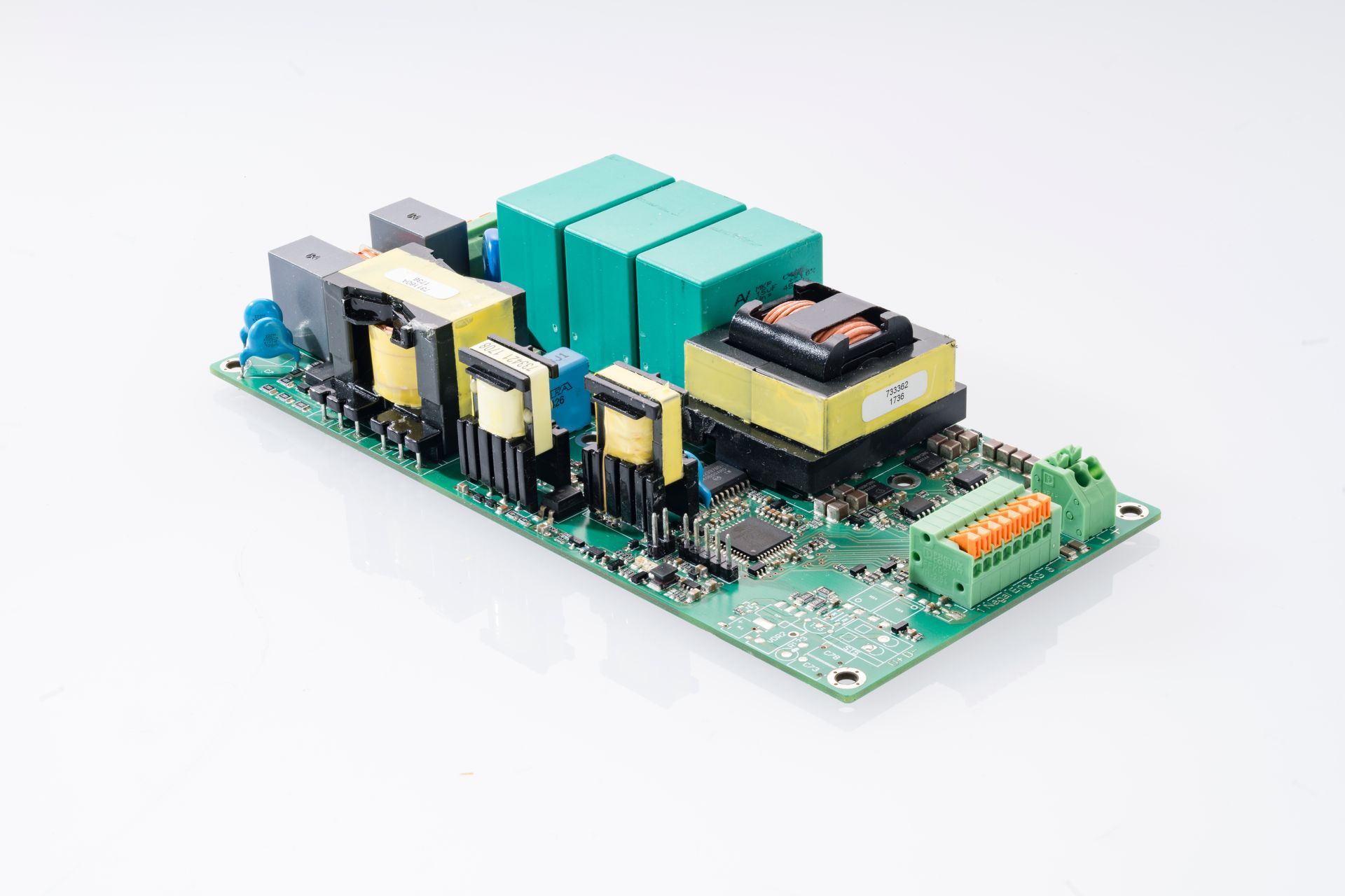 Printed circuit board with multiple electronic components, including transformers, capacitors and terminal blocks. Green and yellow components on a green board.