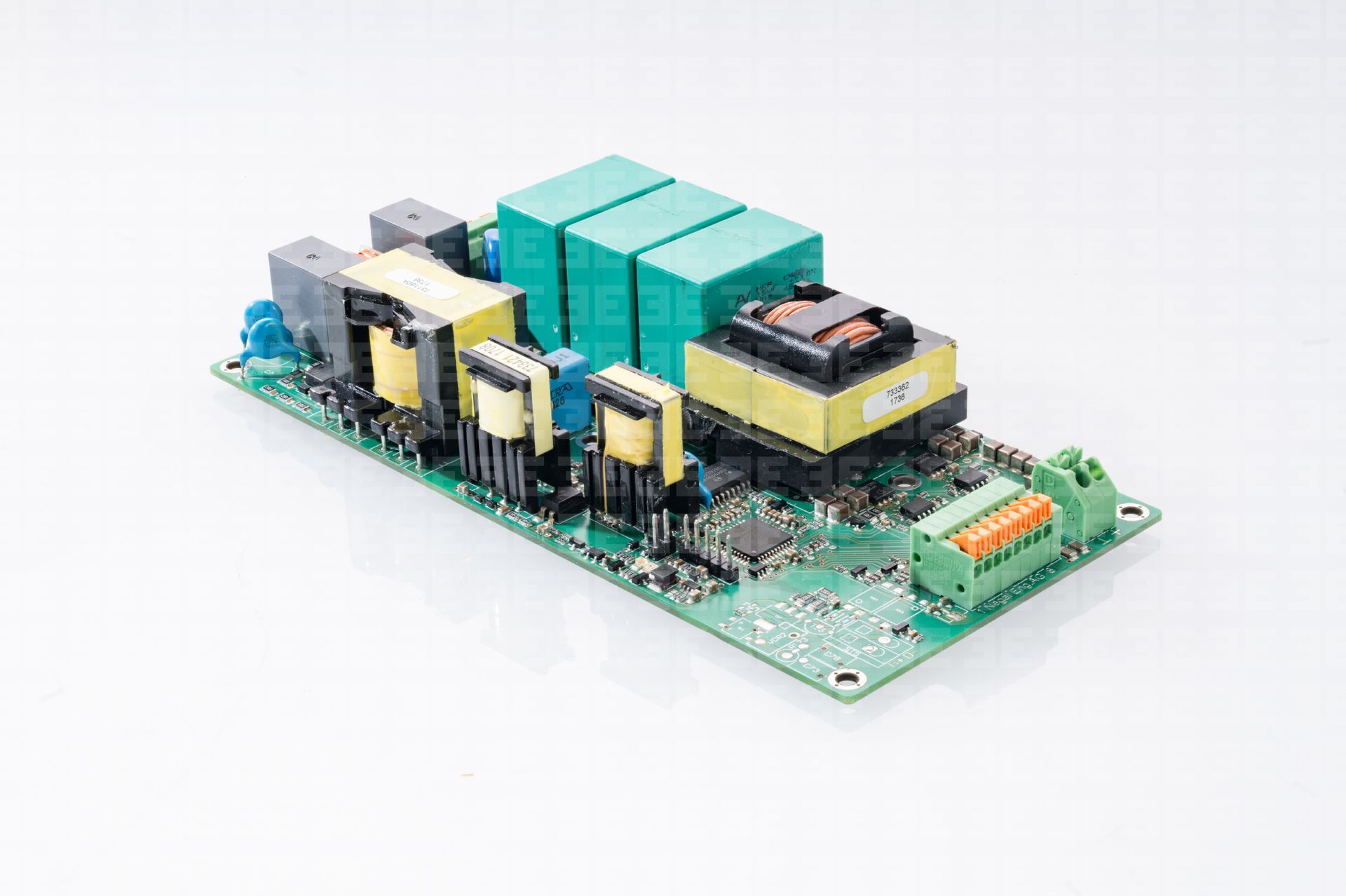 Leiterplatte mit mehreren elektronischen Komponenten, darunter Transformatoren, Kondensatoren und Klemmenblöcke. Grüne und gelbe Komponenten auf einer grünen Platine.