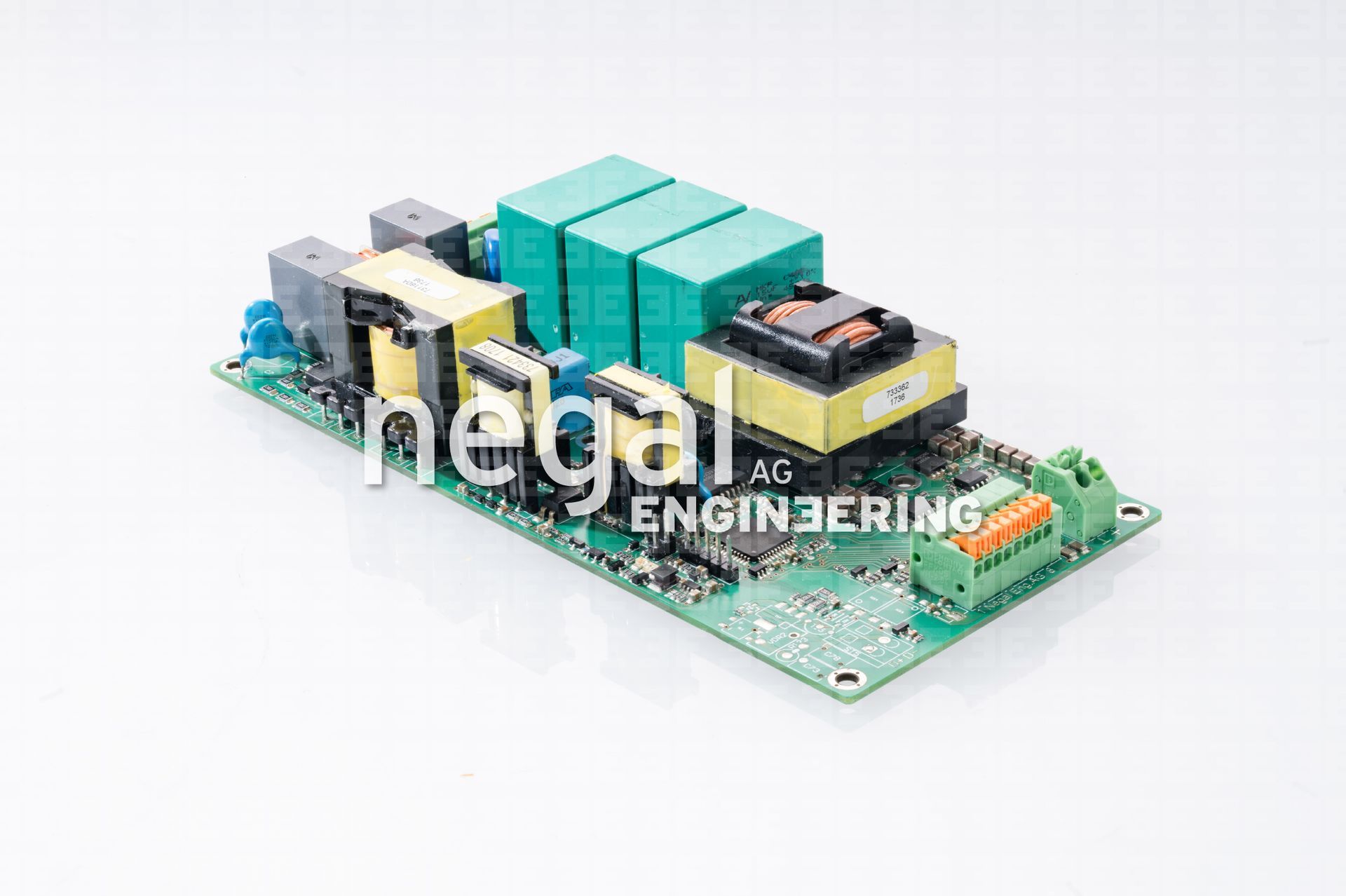 Leiterplatte mit mehreren elektronischen Komponenten, darunter Transformatoren, Kondensatoren und Klemmenblöcke. Grüne und gelbe Komponenten auf einer grünen Platine.