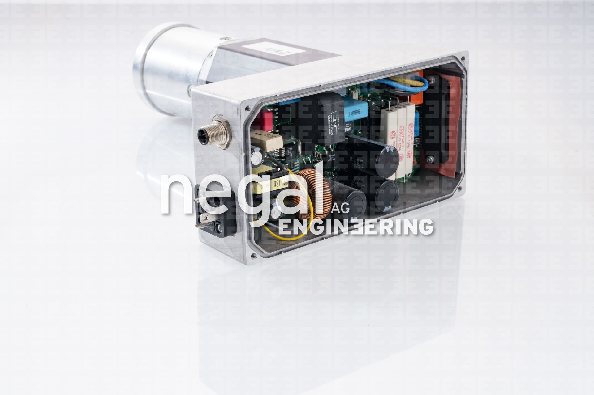 Geöffnetes elektronisches Metallgerät, das Leiterplatten, Kondensatoren und interne Komponenten zeigt. Das Gerät liegt auf einer weißen Oberfläche.