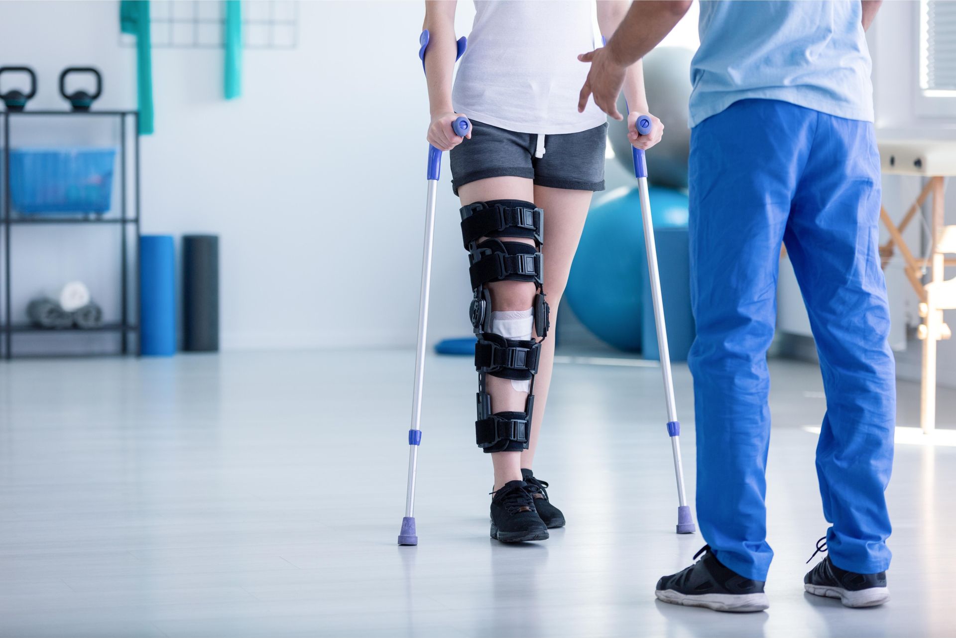 A woman with a knee brace and crutches is being helped by a doctor.