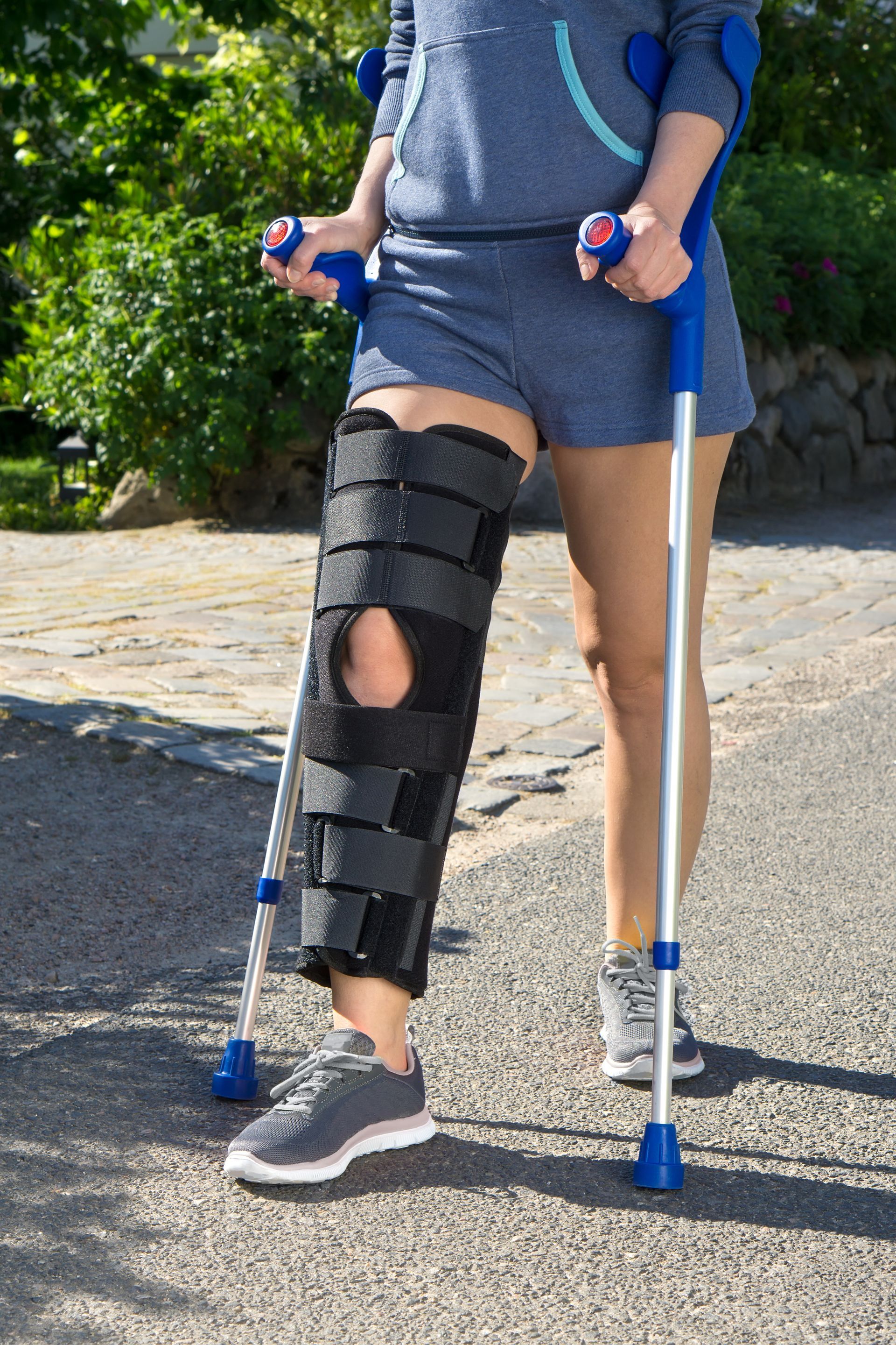 A woman with a knee brace and crutches is walking down the street.