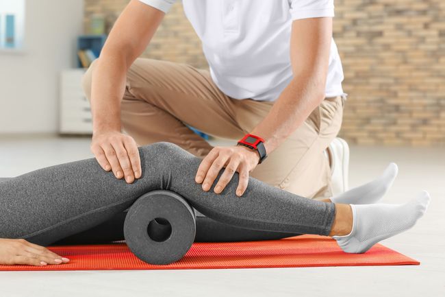 A person is using a foam roller on another person 's leg.