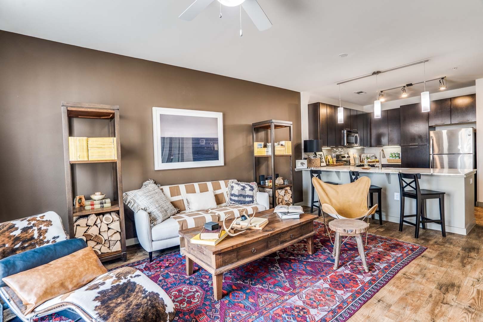 Living room with brown wall, couch, rug, bookshelves, and open kitchen at The Boat House, offers townhomes for rent in  Austin Ranch The Colony, TX.