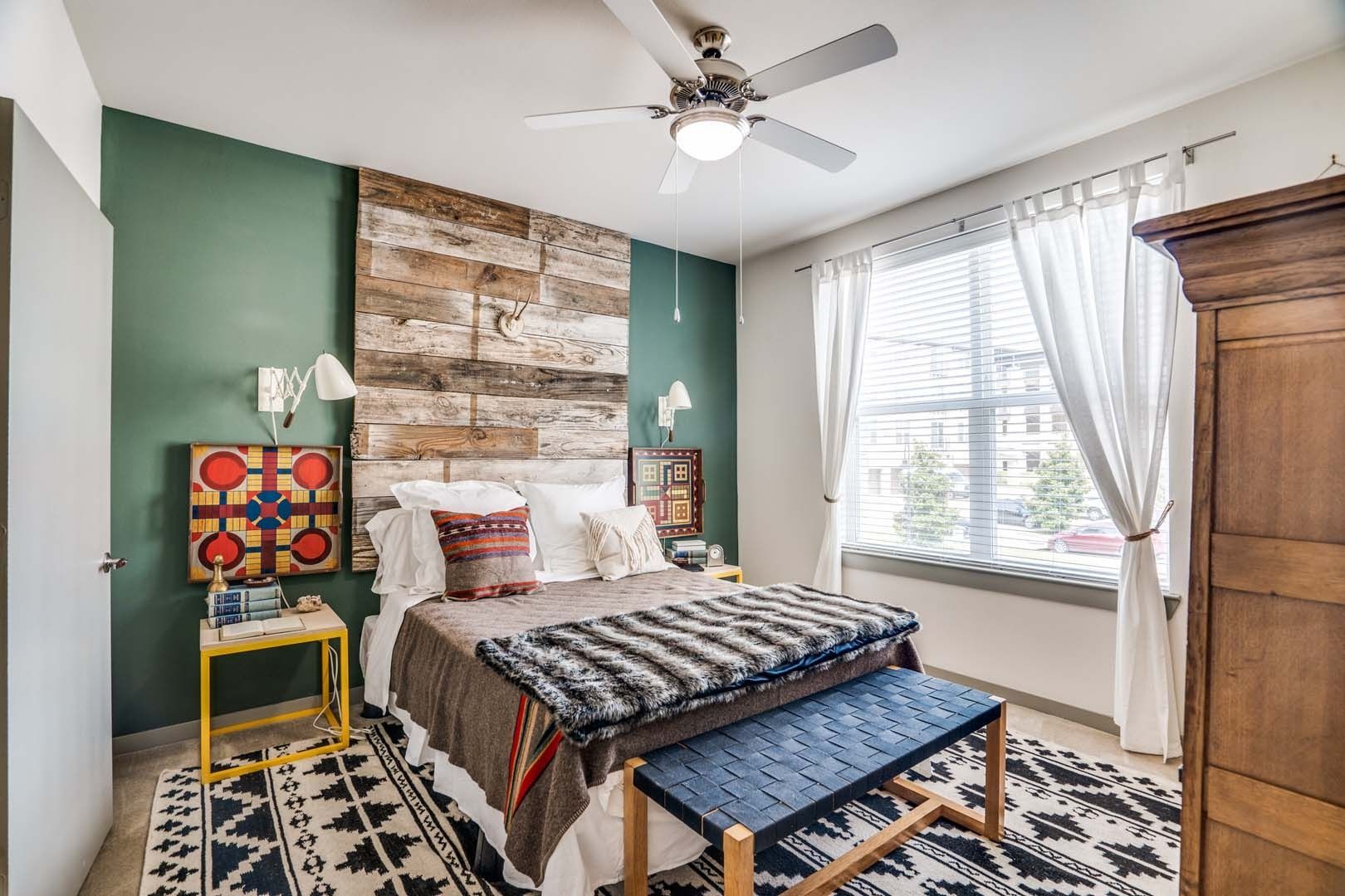 Bedroom with a rustic wood wall, bed with patterned blankets, and a blue bench at The Boat House, offers townhomes for rent in  Austin Ranch The Colony, TX.