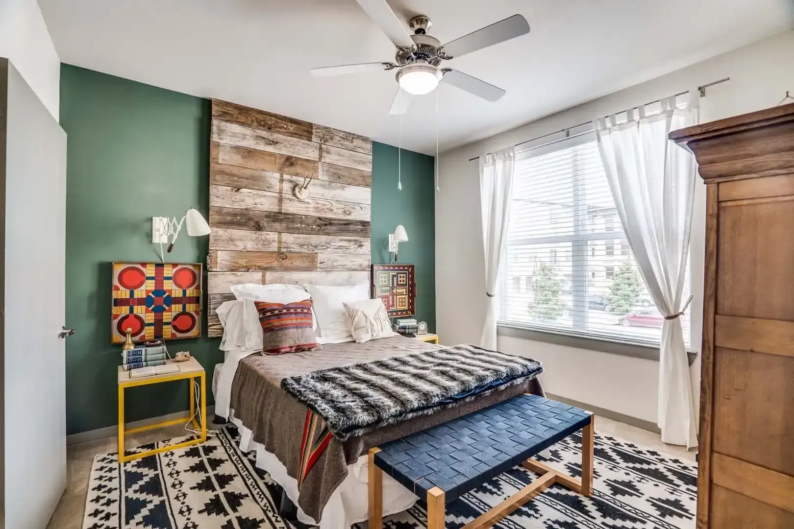 Bedroom with a rustic wood wall, bed with patterned blankets, and a blue bench at The Boat House, offers townhomes for rent in Austin Ranch The Colony, TX.