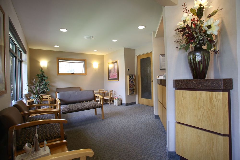 Waiting room with armchairs, a couch, flowers, and a reception desk.