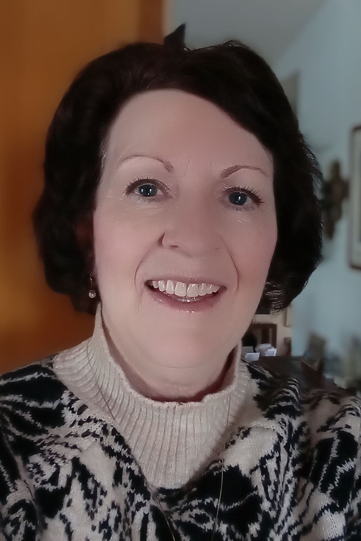 Woman smiling, wearing a patterned sweater, standing indoors.