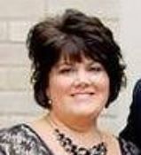 Woman with short, dark hair, wearing a necklace and formal dress, smiling.