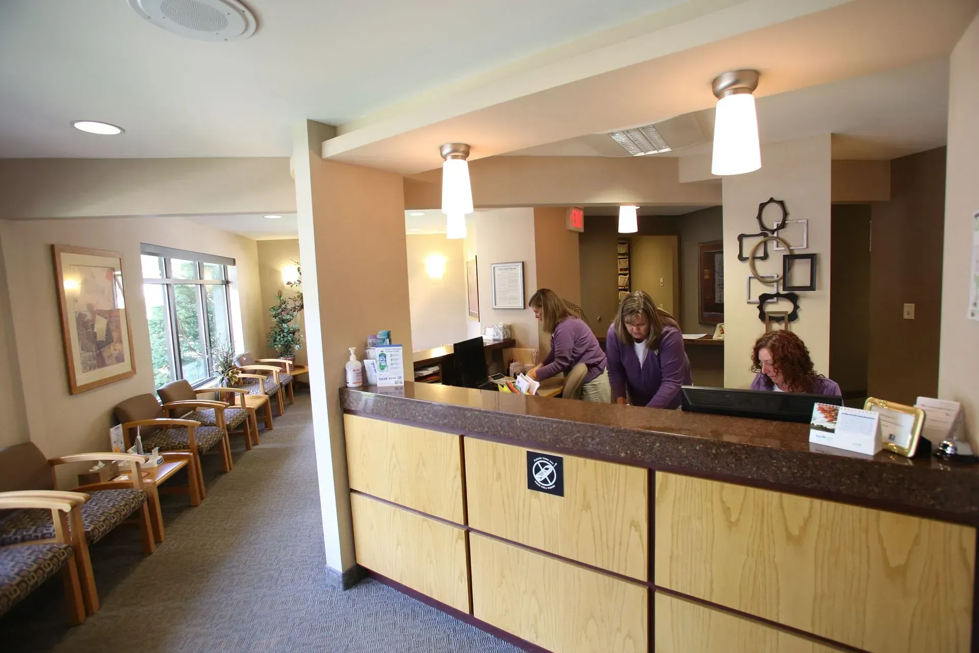 Reception desk in a dental office. Staff members work behind the counter; a waiting area with chairs is on the left.