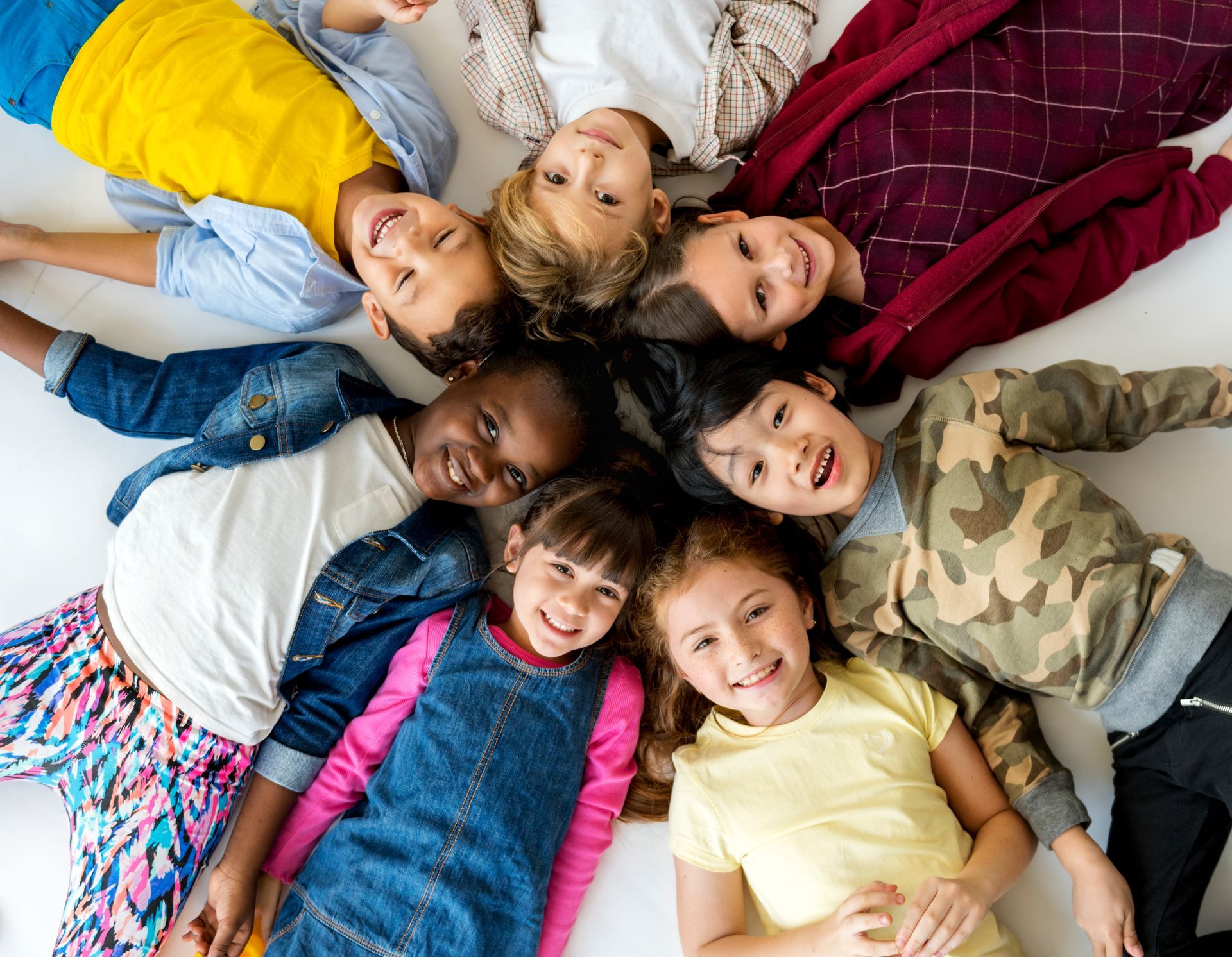 A group of children are laying in a circle on the floor.