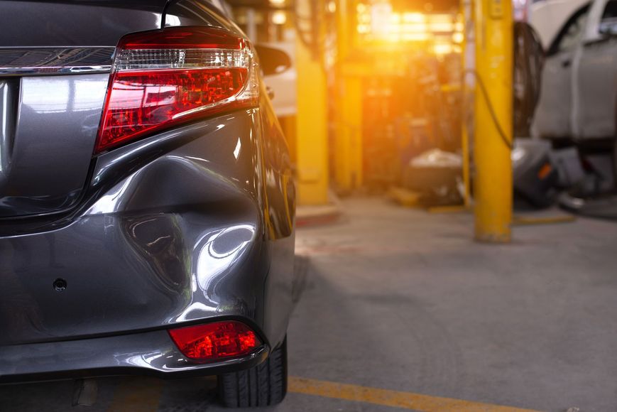 A car with a damaged bumper is parked in a garage.