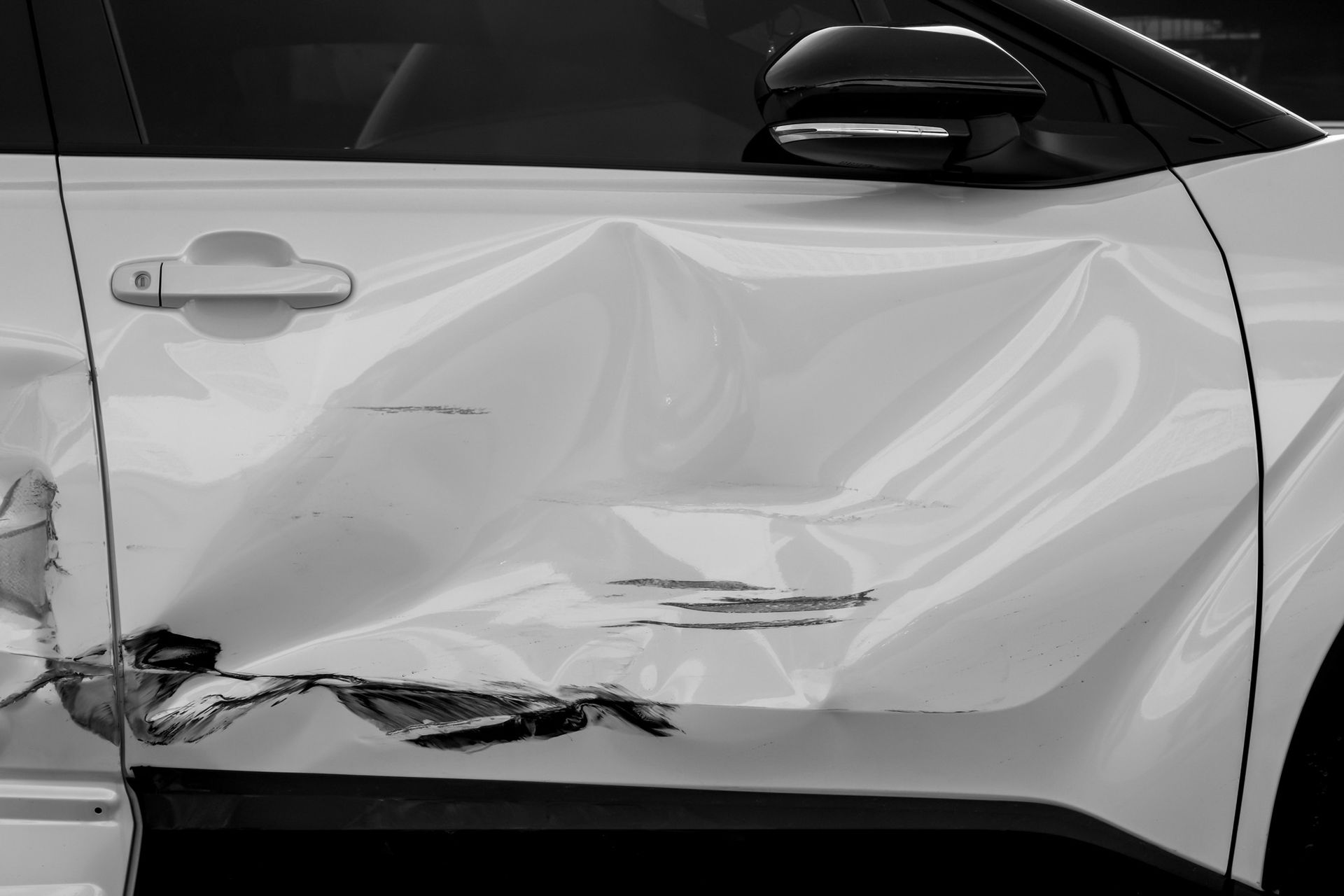 A black and white photo of a white car with a damaged door.