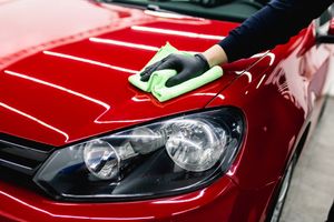 A person is cleaning a red car with a green cloth.