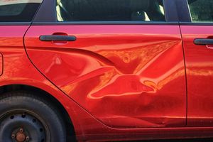 A red car with a damaged door is parked on the side of the road.