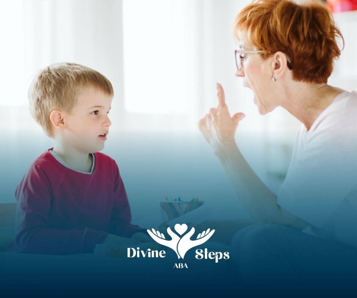 ABA therapist interacting with a young autistic boy at a table, holding flashcards.