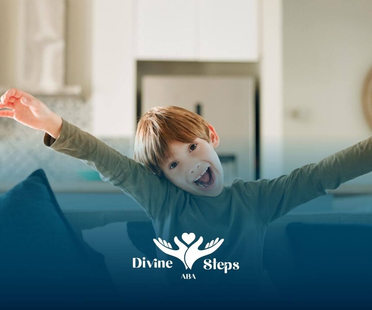 A young boy with autism on a couch with arms raised, smiling excitedly.