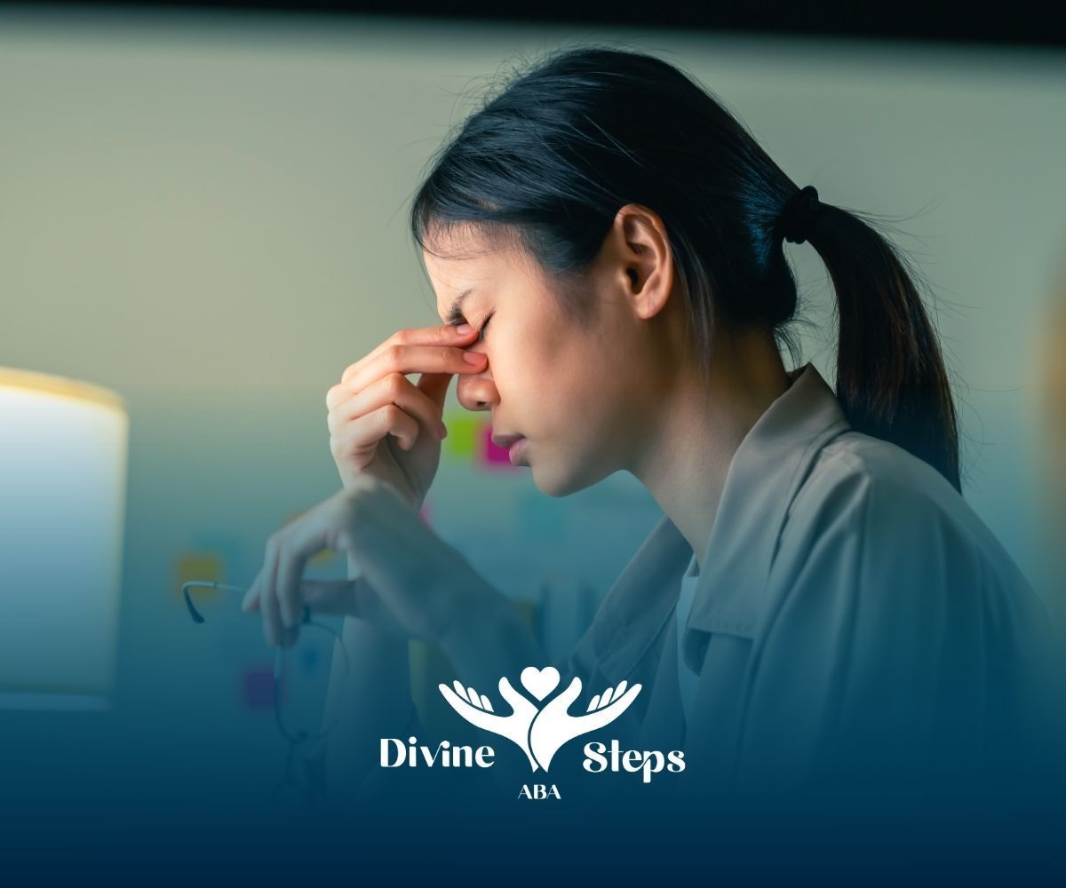 Woman with hand on face, appears stressed, indoors at a desk, light source visible.