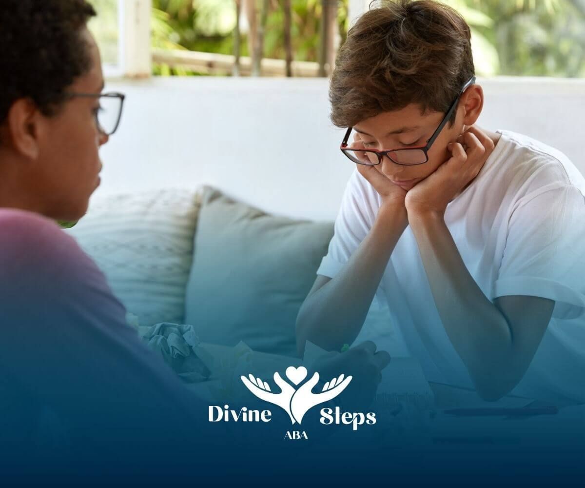 Two autistic kids working together at a table, one offering guidance while the other concentrates.