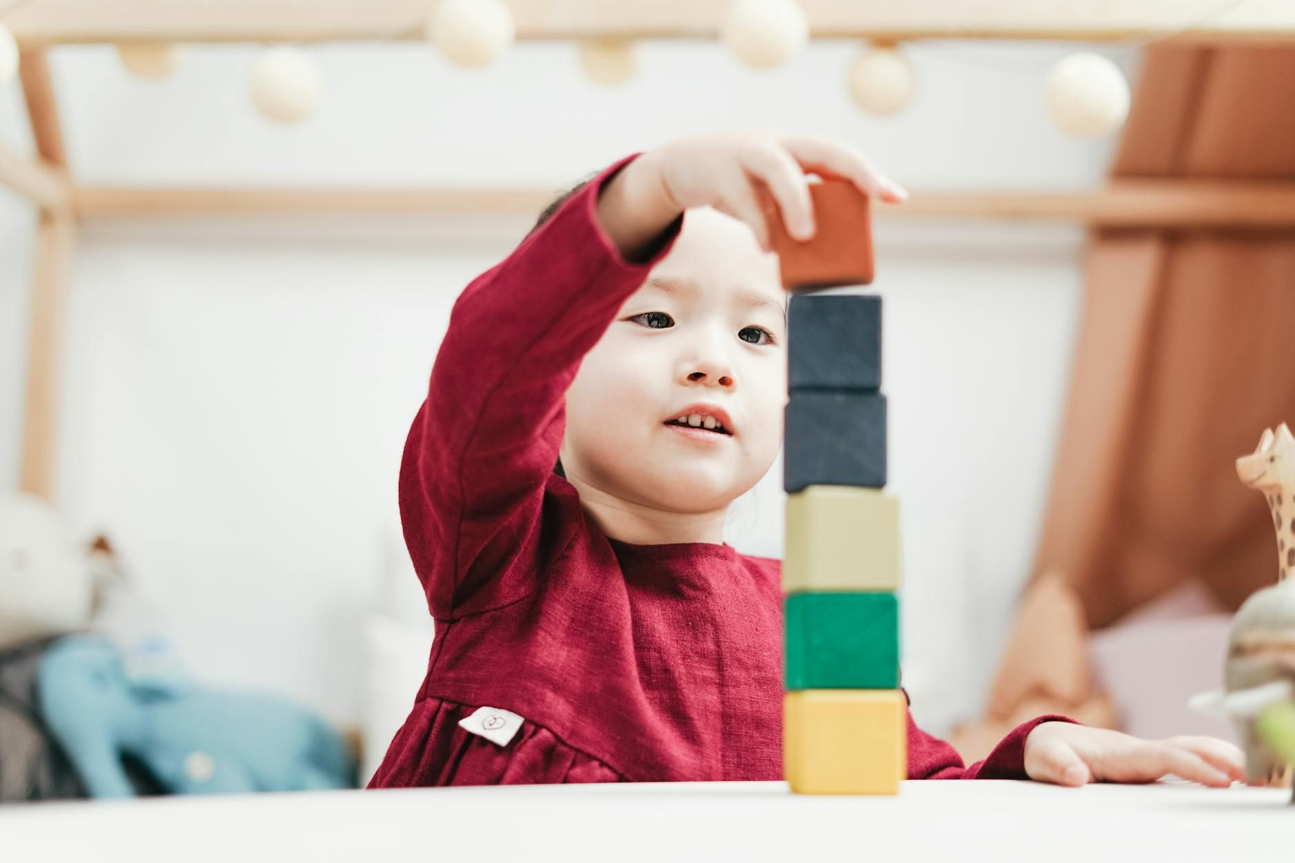 An autistic child in red dress stacking colorful blocks on a table during in-home ABA therapy in MD.