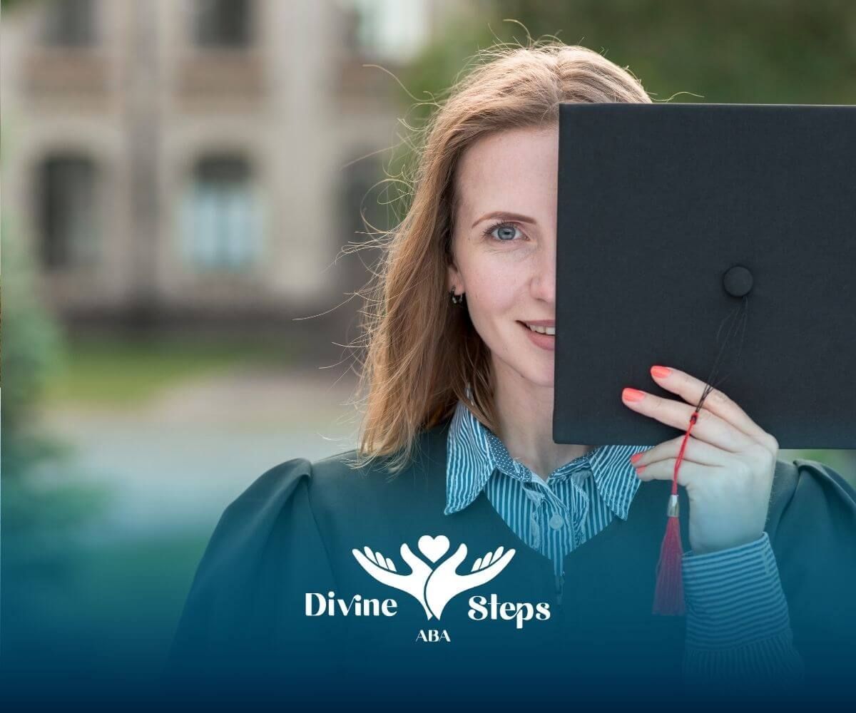 A student in a black graduation gown, smiling while holding a graduation cap in front of her face.